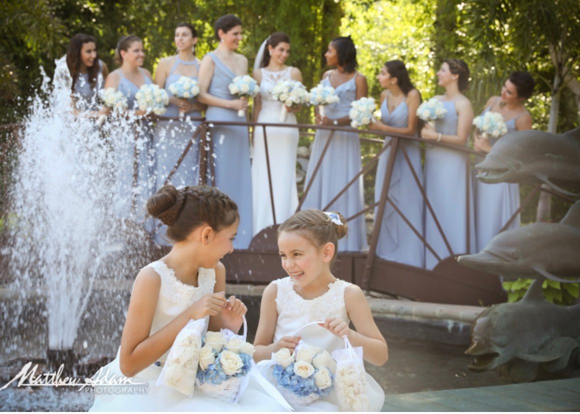 flower girls in photo, with bridal party behind them on a bridge