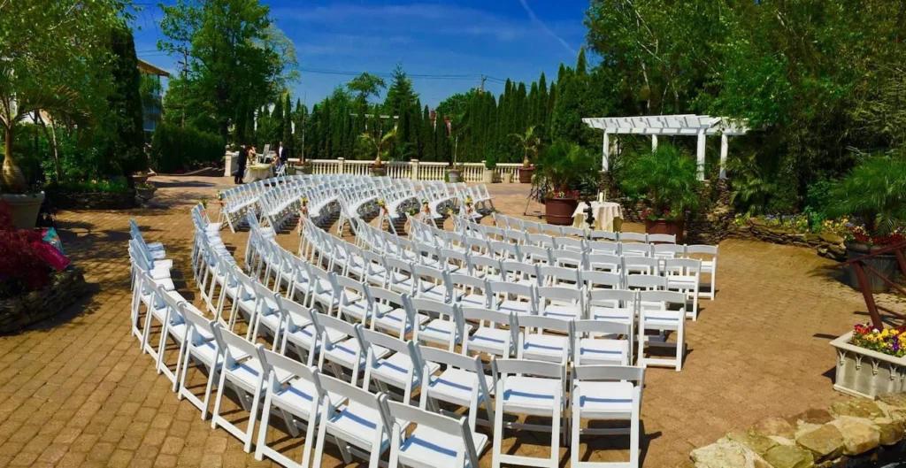 Outdoor wedding ceremony setup with rows of white chairs facing a gazebo surrounded by trees and greenery.