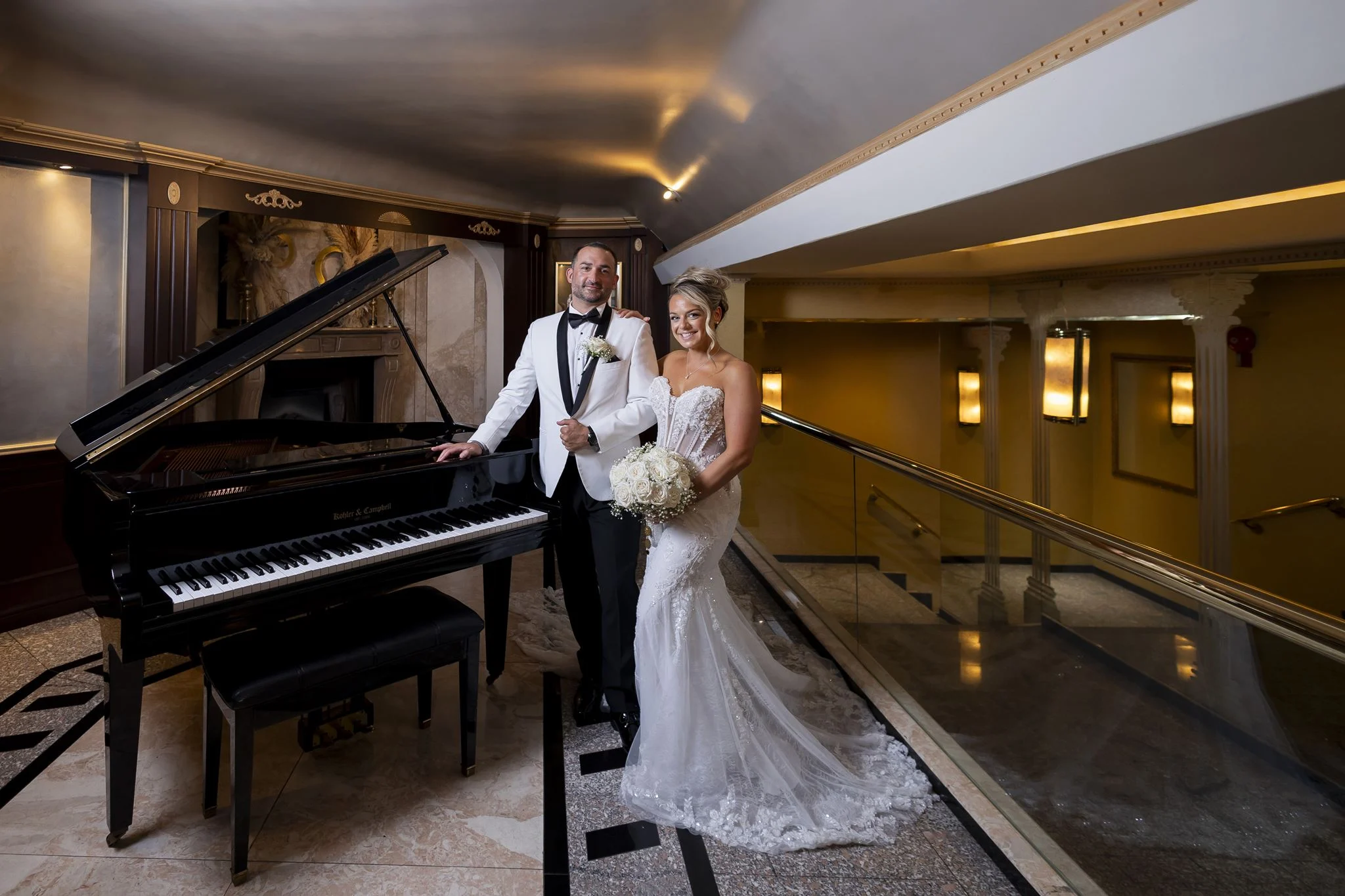 Bride and groom posing beside a grand piano in an elegant indoor wedding venue.